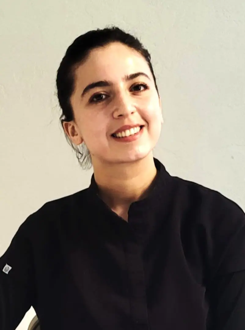 Smiling person in dark clothing, neutral background.